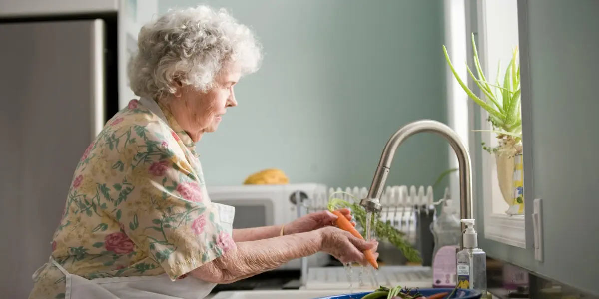 Older Woman At Window Washing a Carrot